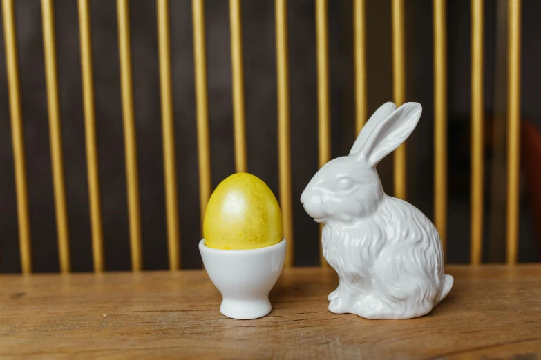 a white rabbit sitting next to a yellow egg, inspired by Sarah Lucas, white finish, silver egg cup, battered, handcrafted