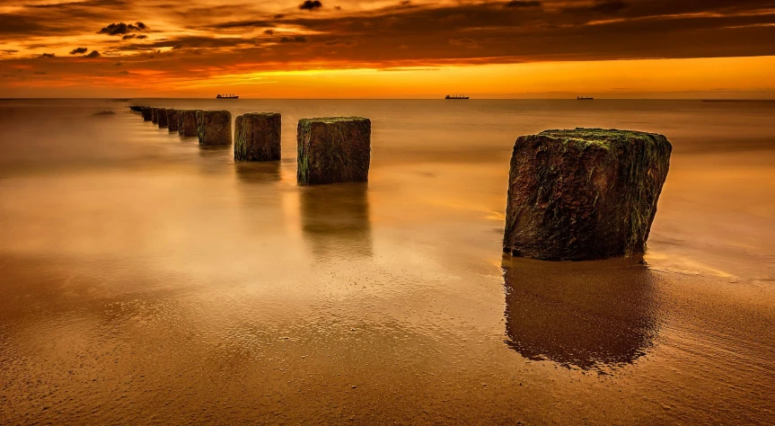 a group of wooden posts sitting on top of a sandy beach, by Andries Stock, pexels contest winner, orange skies, floating rocks, ships, today\'s featured photograph 4k