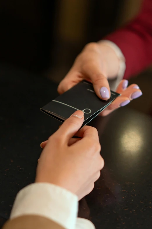 a close up of a person holding a cell phone, on a table, black paper, pair of keycards on table, thumbnail