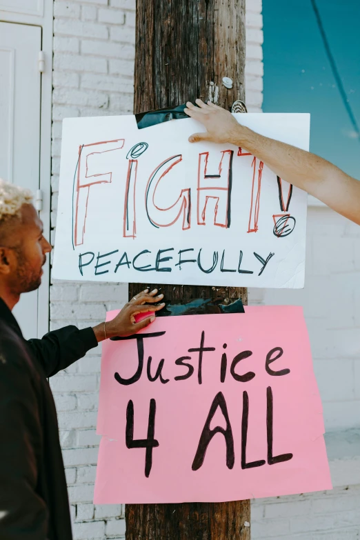 a woman standing next to a man holding a sign, by Jessie Algie, pexels, black arts movement, two men hugging, at peace, fights, instagram story