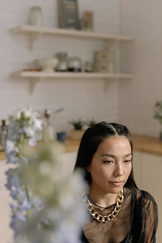 a woman sitting at a table with a plate of food, flowers in her dark hair, gemma chen, looking serious, profile image