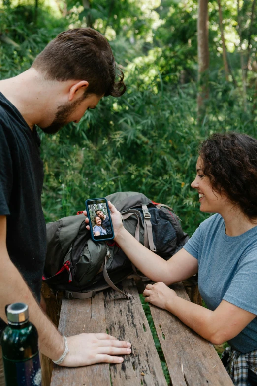 a man and a woman sitting at a picnic table, a picture, pexels contest winner, happening, holding a very advance phone, 4k trailcam, a man wearing a backpack, avatar image