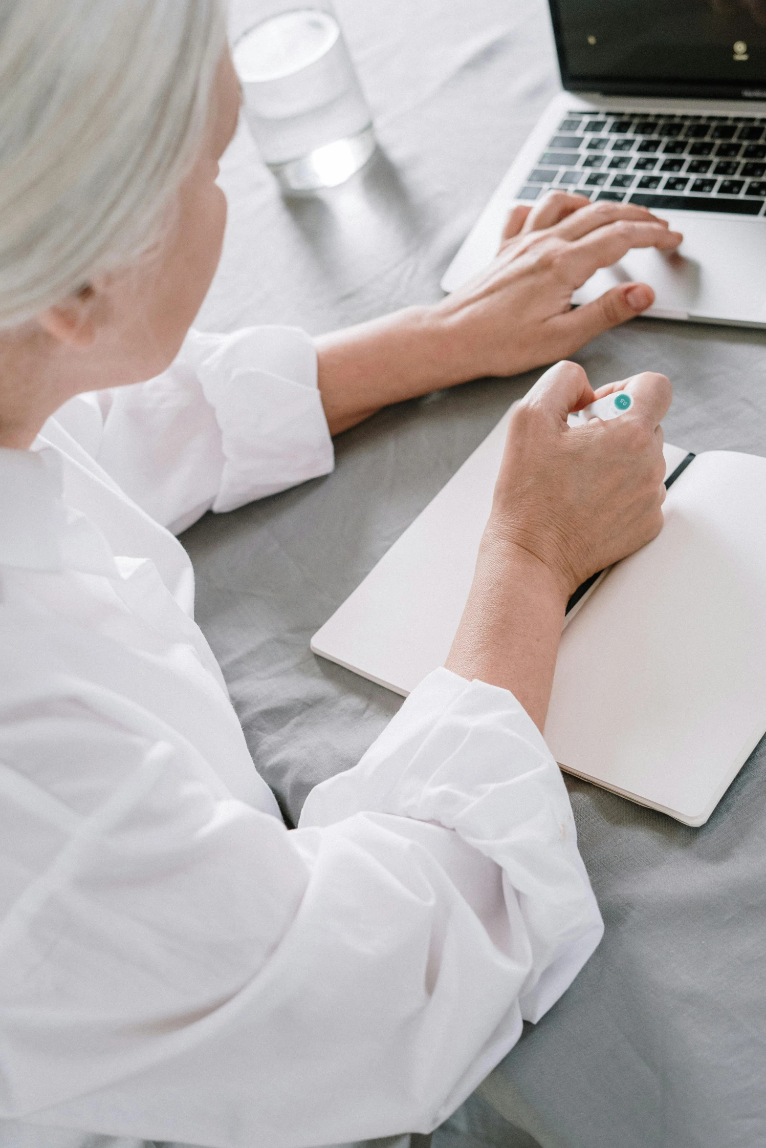 a woman sitting at a table working on a laptop, inspired by Agnes Martin, white and teal garment, white hair color, scrolling computer mouse, scientific research