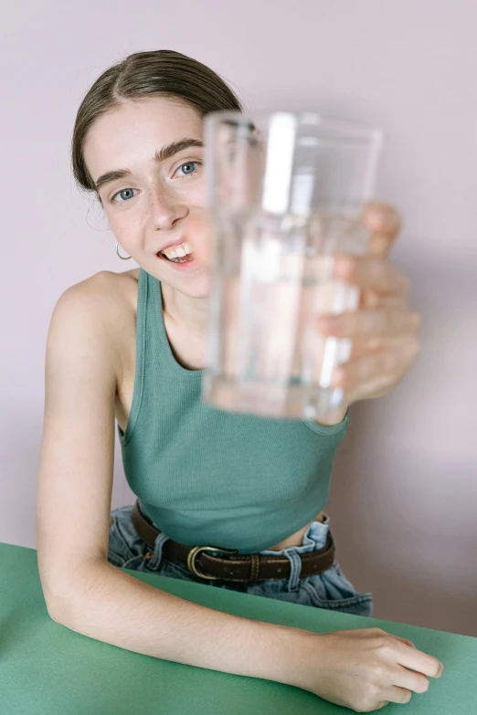 a woman sitting at a table holding a glass of water, resembling a mix of grimes, wearing a tanktop, high quality photo, close-up photograph
