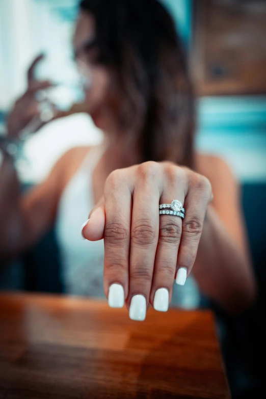 a woman sitting at a table with a ring on her finger, zoomed in shots, crystals and diamonds, with a drink, clean and pristine design