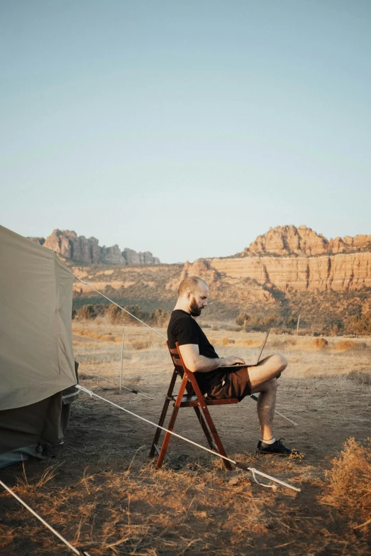 a woman sitting in a chair in front of a tent, by Lee Loughridge, trending on unsplash, renaissance, bald man, moab, handsome man, conde nast traveler photo