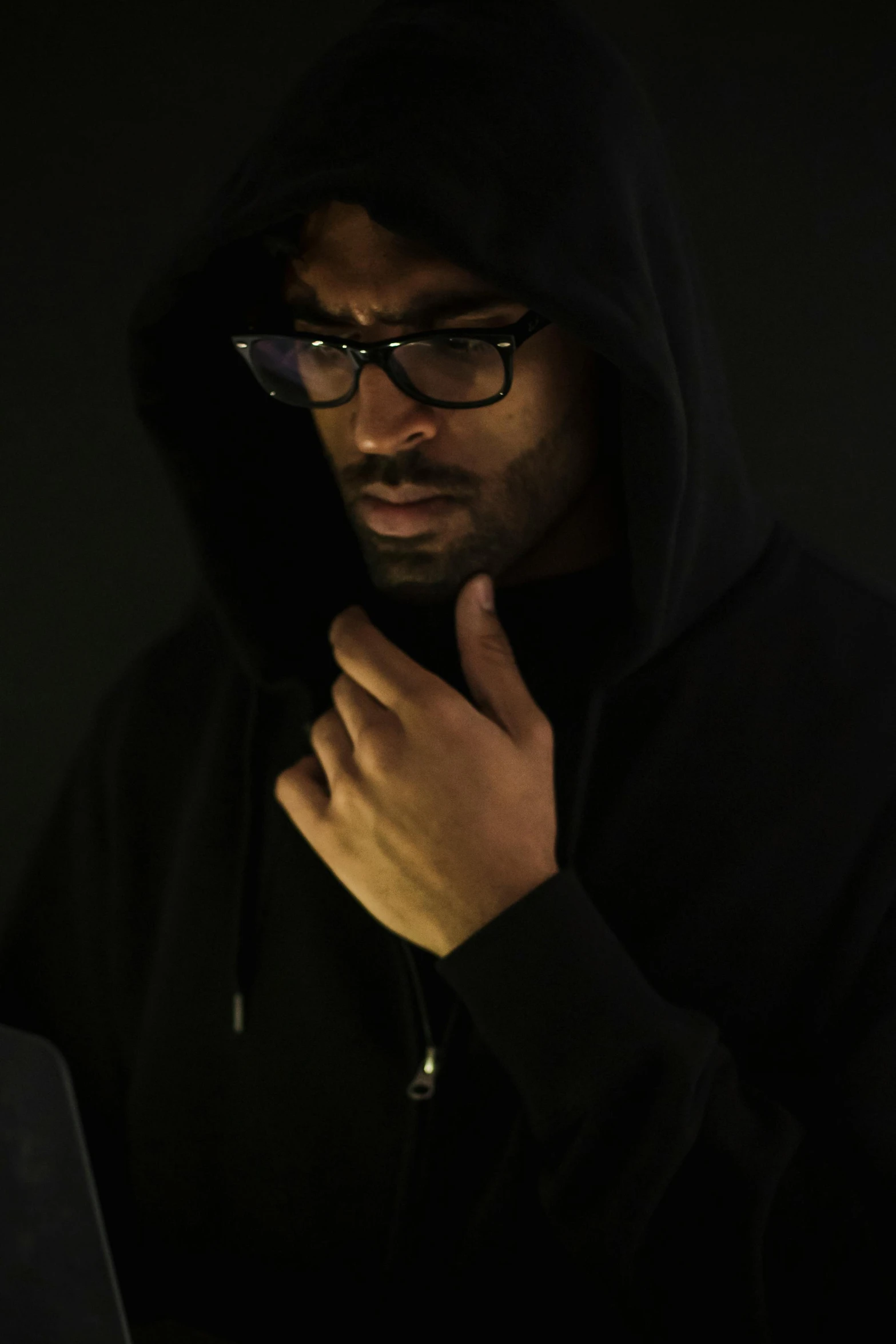 a man sitting in front of a laptop computer, an album cover, by Stokely Webster, black hoodie techie, ( ( theatrical ) ), man with glasses, dramatic press photo