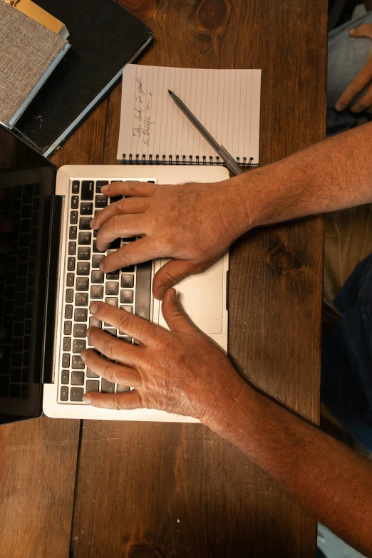 a man sitting at a table using a laptop computer, by Carey Morris, pexels, top-down shot, closeup of arms, rustic, teaching