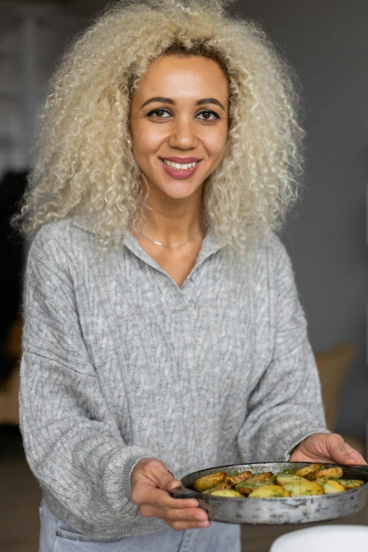 a woman holding a plate of food in a kitchen, a character portrait, pexels contest winner, hurufiyya, curly blond hair, on grey background, aida muluneh, wearing casual clothing