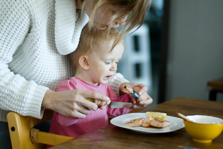 a woman feeding a baby food at a table, pexels contest winner, salmon, eating garlic bread, manuka, eva elfie