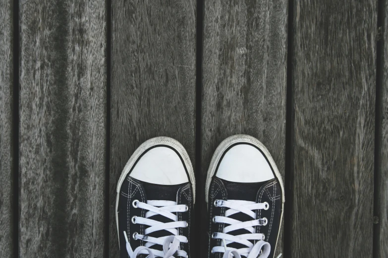 a pair of black sneakers sitting on top of a wooden floor, a black and white photo, pexels contest winner, dressed in a worn, deck, with a white, a wooden