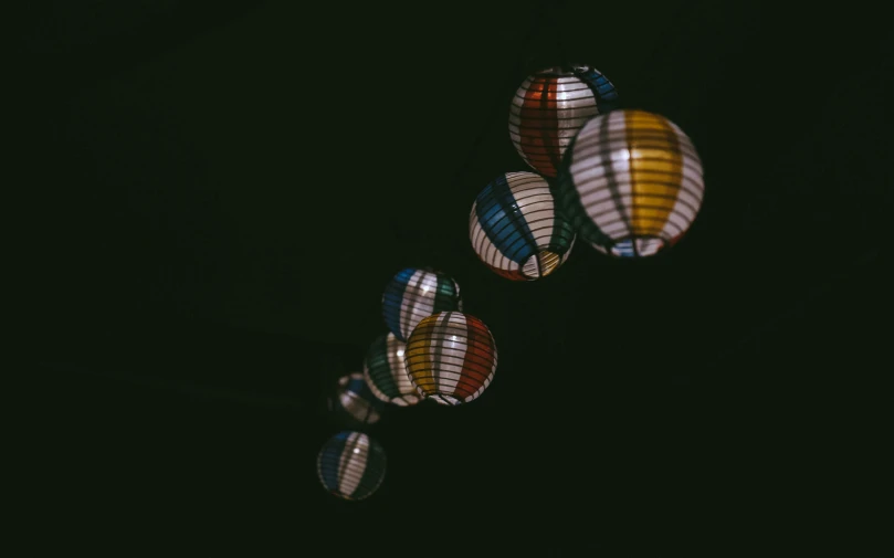 a couple of balloons that are in the air, by Matija Jama, unsplash, light and space, japan at night, lantern, colored analog photography, with a black background