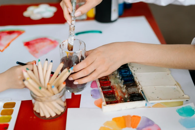 a group of people that are painting on a table, a watercolor painting, trending on pexels, red brown and white color scheme, child's drawing, colorful glass art, holding pencil