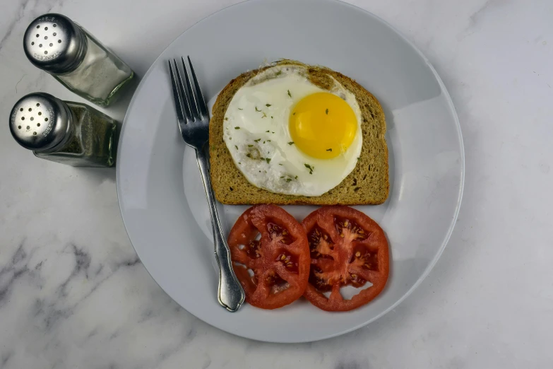 a white plate topped with a piece of bread and a fried egg, also one tomato slice, detailed product image, fan favorite, translucent eggs