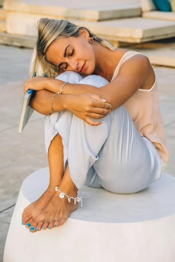 a woman sitting on top of a white stool, wearing two silver bracelets, oceanside, laid - back, thinker pose
