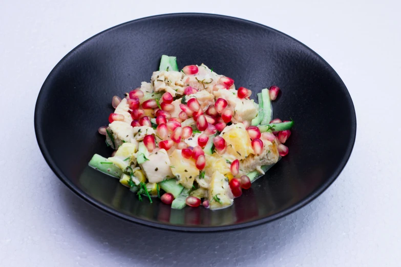 a black plate topped with a salad covered in pomegranate, a pastel, by Jessie Algie, bowl, pearlized, on grey background, square