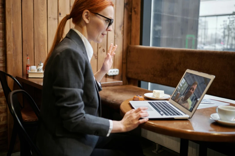 a woman sitting at a table with a laptop, trending on pexels, hr ginger, lachlan bailey, wearing a suit and glasses, thumbnail