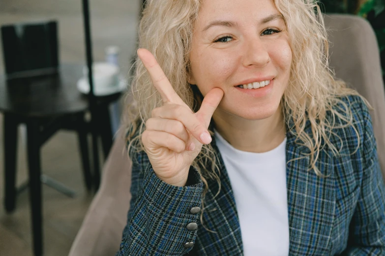 a woman sitting at a table with a plate of food, giving the middle finger, pale skin curly blond hair, professional profile picture, zoomed in
