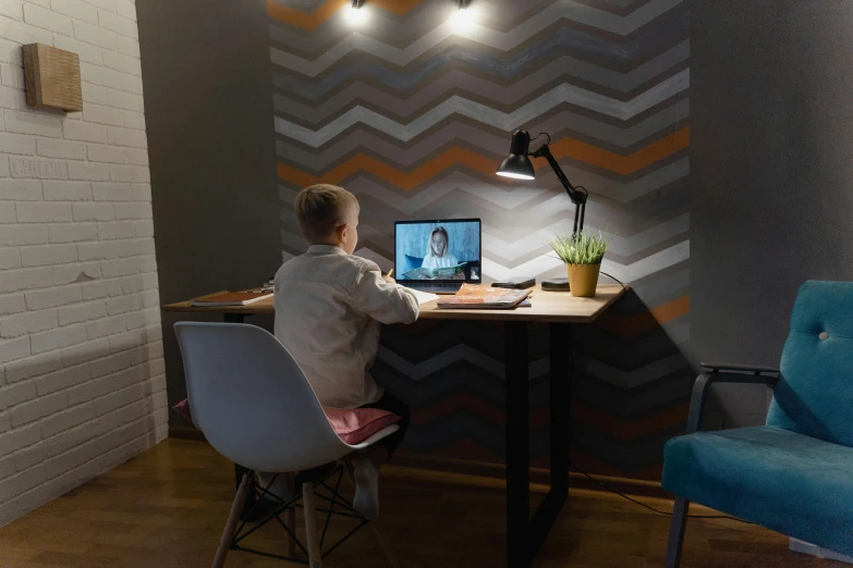 a boy sitting at a desk in front of a laptop computer, inspired by Alexander Roslin, pexels contest winner, video art, room lighting, small and cosy student bedroom, white accent lighting, high - angle view