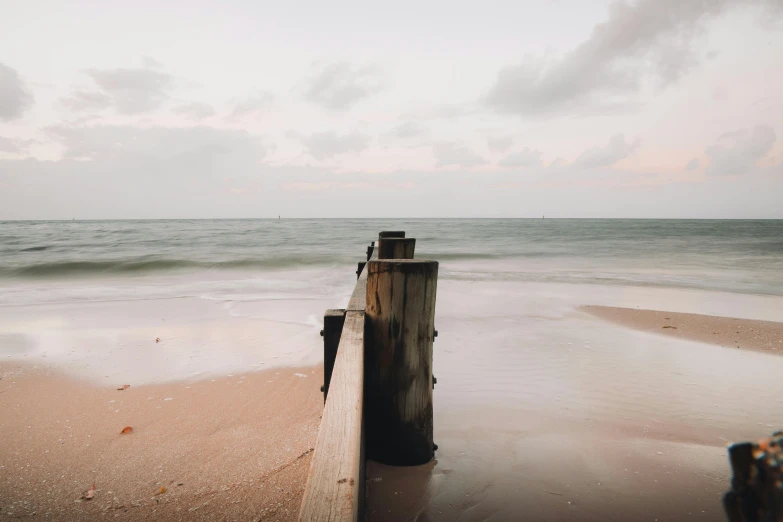 a wooden post sitting on top of a sandy beach, a picture, unsplash contest winner, overcast dusk, near a jetty, instagram post, muted browns