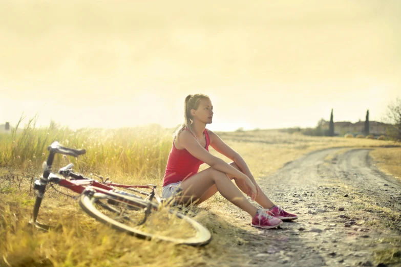 a woman sitting on the side of a dirt road next to a bike, sun drenched, avatar image, sports photo, getty images