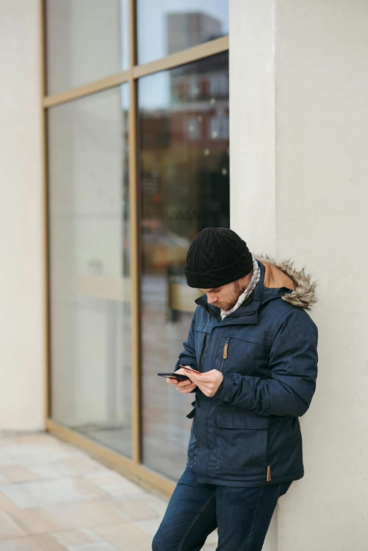 a man leaning against a wall using a cell phone, pexels, cold weather, inspect in inventory image, without text, wearing jacket