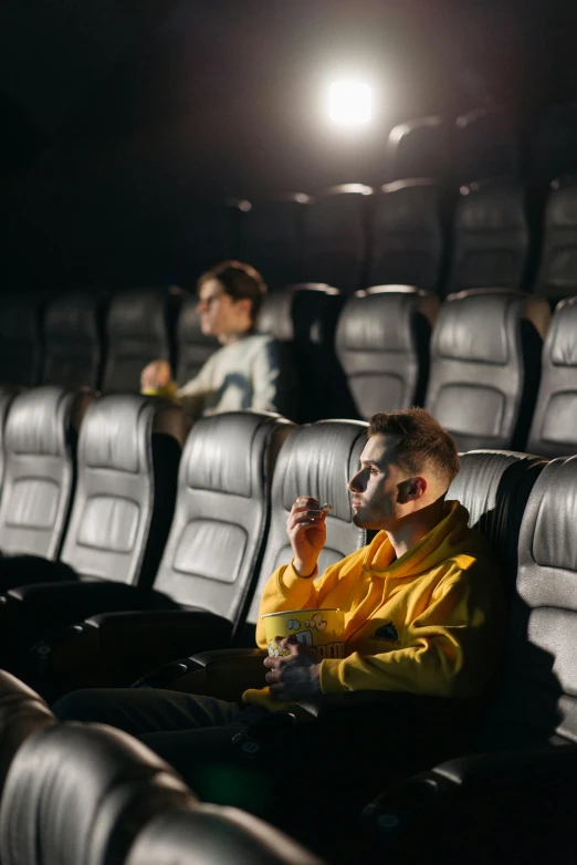a man in a yellow jacket sitting in a movie theater, trending on pexels, [ theatrical ]