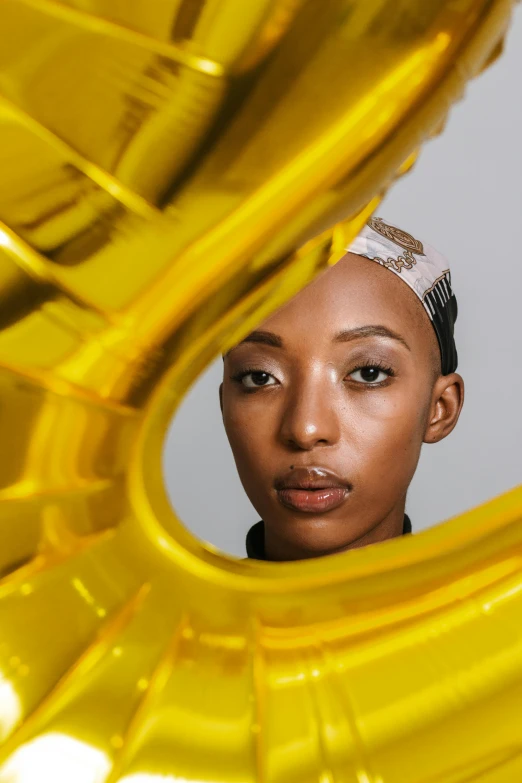 a woman holding a gold balloon in front of her face, by artist, trending on unsplash, afrofuturism, a portrait of issey miyake, horns, shot with sony alpha 1 camera, ashteroth