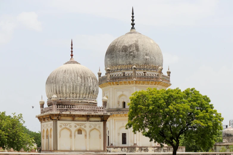 a man sitting on a bench in front of a building, a marble sculpture, with great domes and arches, indiecraft aesthetic, twins, overlooking