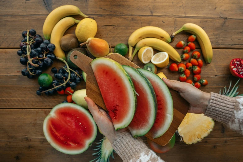 a person cutting up slices of watermelon on a cutting board, by Niko Henrichon, pexels contest winner, figuration libre, background image, tropical fruit, multicoloured, vegetables on table and candle