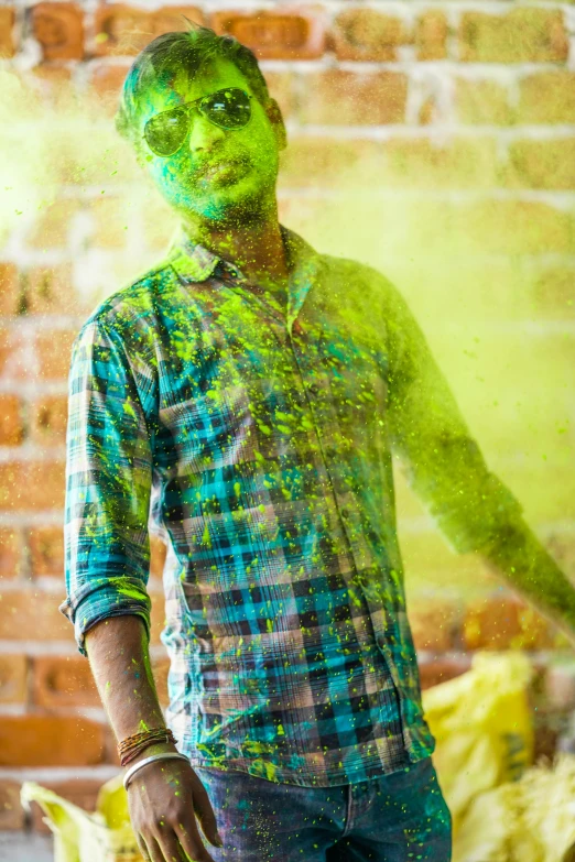 a man standing in front of a brick wall, action painting, magical sparkling colored dust, green shirt, colour print, festive colors