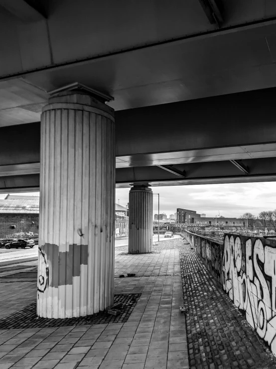 a black and white photo of a street under a bridge, inspired by Thomas Struth, unsplash, graffiti, giant columns, hannover, view, abandoned shopping mall