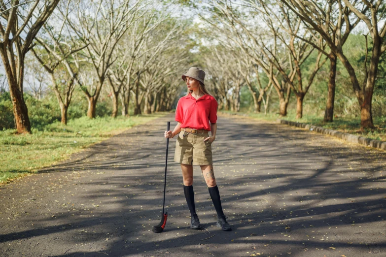 a woman standing in the middle of a road with a walking stick, by Julia Pishtar, wearing golf shorts, in a jungle, red uniform, instagram post