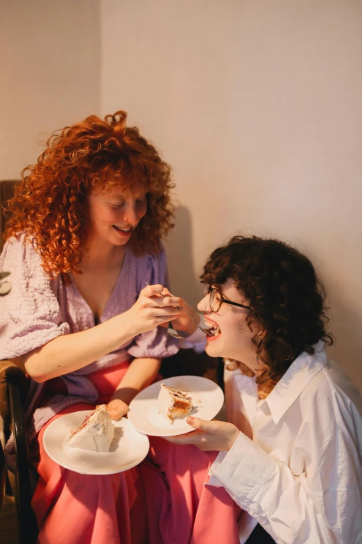 a couple of women sitting next to each other, a portrait, inspired by Nan Goldin, pexels, eating cakes, with curly red hair, andy milonakis, serving happy meals