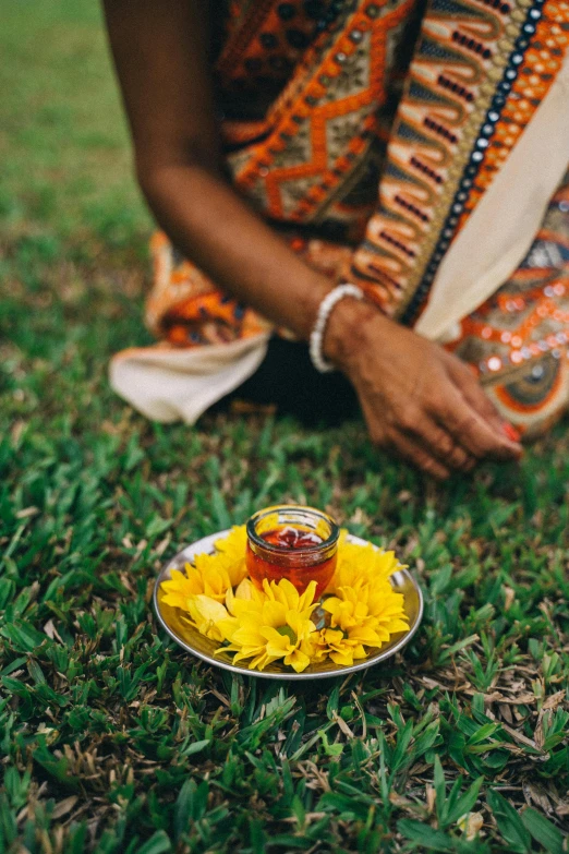 a person sitting in the grass with a plate of food, kalighat flowers, holding hot sauce, pray, uncropped