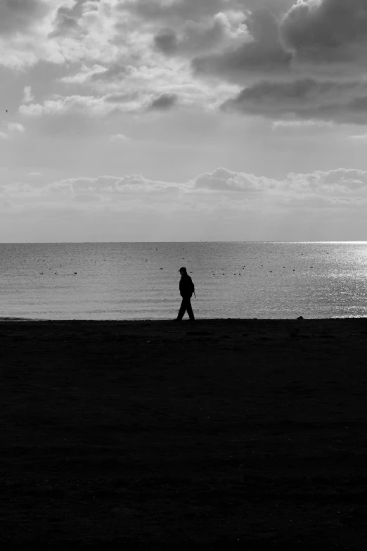 a black and white photo of a person walking on the beach, character silhouette, brooding, silhouette :7, black & white photo