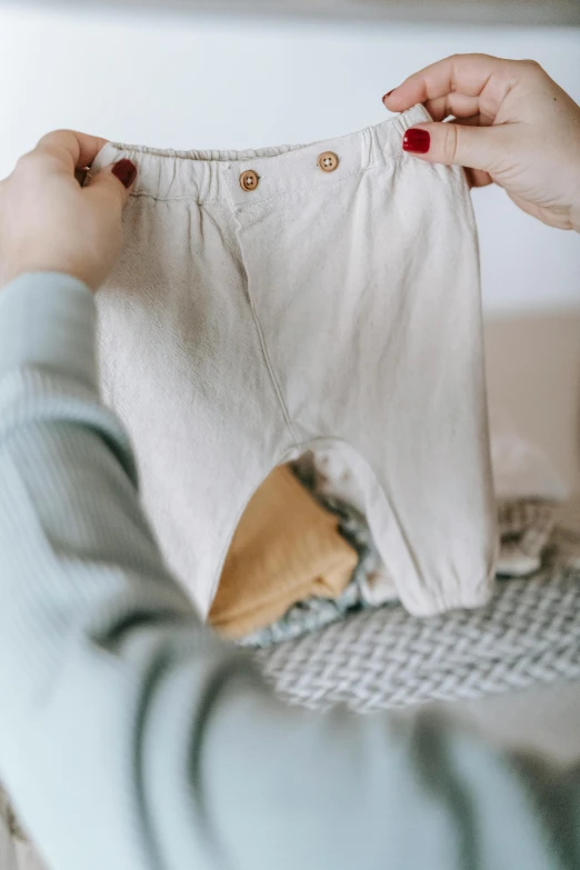 a close up of a person holding a pair of pants, by Nicolette Macnamara, trending on pexels, diaper-shaped, wearing a linen shirt, childish look, creating a soft