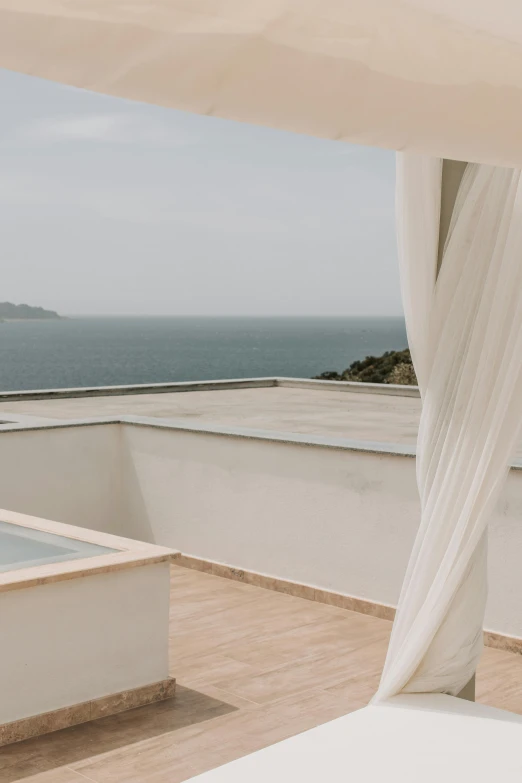 a white bed sitting on top of a wooden floor, inspired by Tomàs Barceló, hills and ocean, shot from roofline, canopies, white travertine terraces