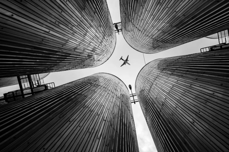 a black and white photo of a plane flying in the sky, by Tobias Stimmer, pexels contest winner, conceptual art, rusty metal towers, silo, vertical lines, turkey