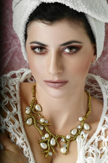 a woman with a white towel on her head, inspired by Gabriel Ba, baroque, gemstone necklace, shades of gold display naturally, photo of a model, real pearls