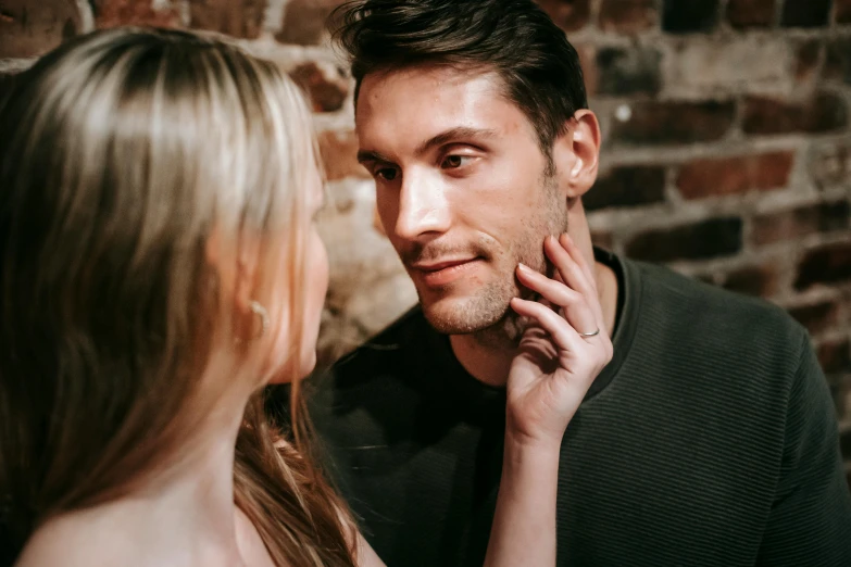 a man standing next to a woman in front of a brick wall, by Adam Marczyński, trending on pexels, renaissance, square masculine jaw, looking in mirror, flirting, slight stubble