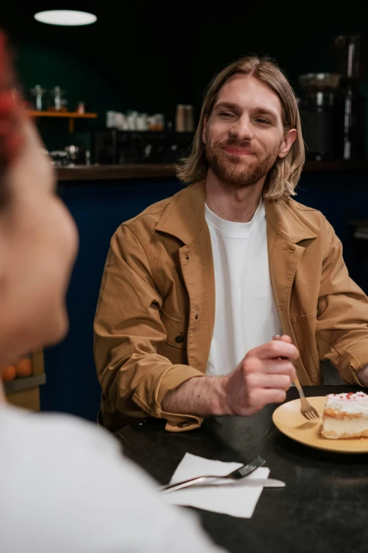 a man sitting at a table with a plate of food, cake in hand, looking at each other mindlessly, aussie baristas, blonde man