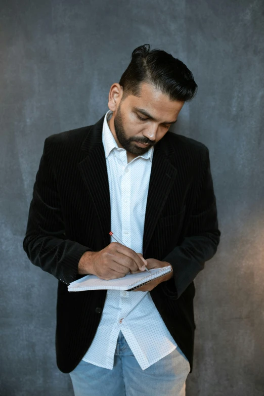 a man in a suit writing on a piece of paper, an album cover, inspired by Germán Londoño, pexels contest winner, a portrait of rahul kohli, studious chiaroscuro, fullbody or portrait, islamic