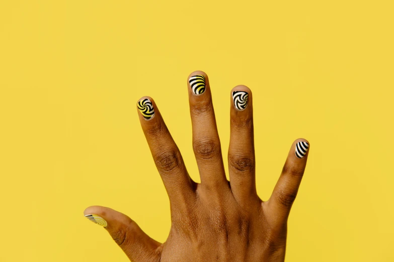 a close up of a person's hand with black and white nails, inspired by Ras Akyem, op art, yellow magic theme, swirl, yoruba body paint, waving at the camera