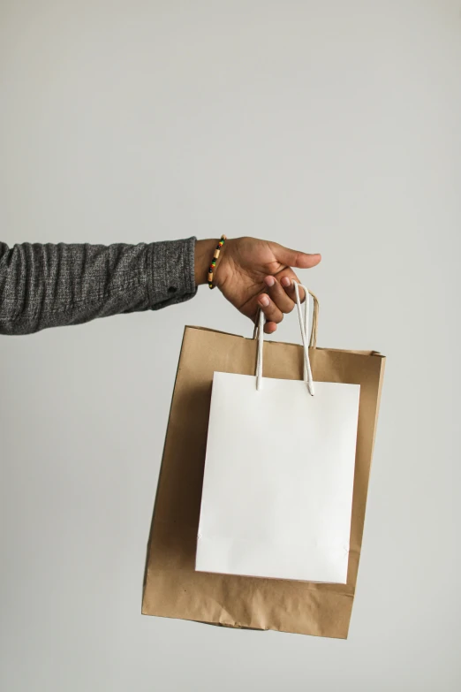 a person holding a shopping bag in their hand, pexels contest winner, minimalism, white sleeves, gold, thumbnail, brown paper