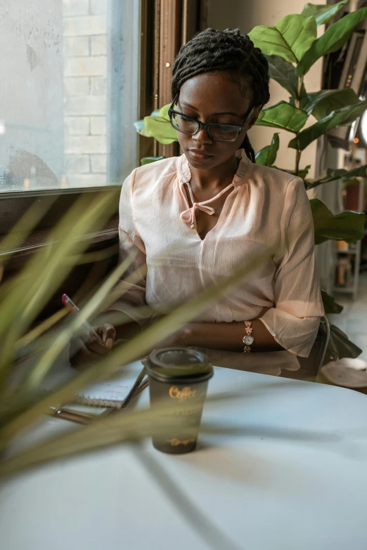 a woman sitting at a table in front of a laptop, trending on unsplash, ethiopian, woman with rose tinted glasses, sitting alone in a cafe, photographed for reuters