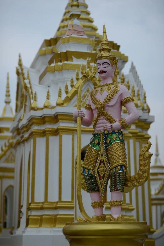 a close up of a statue in front of a building, a temple, pink and gold, in style of thawan duchanee, man holding spear