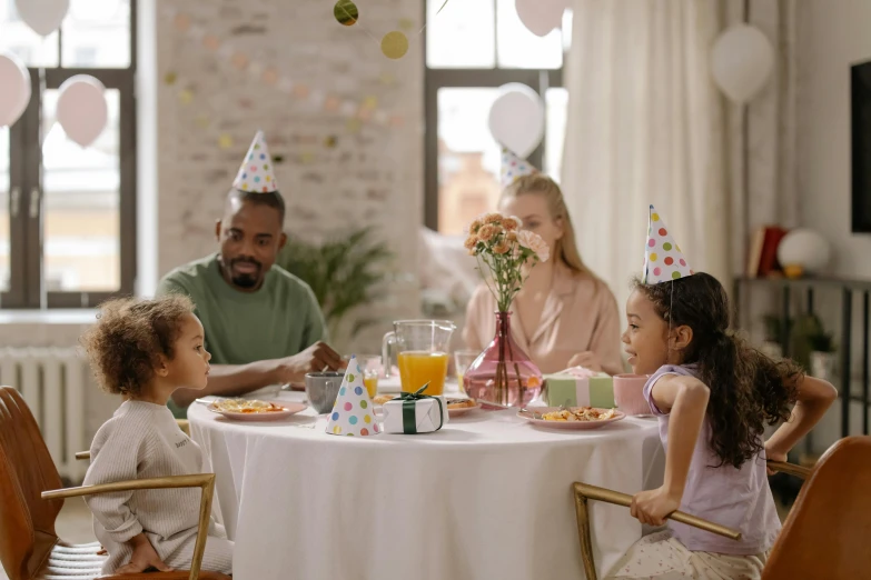 a group of people sitting around a table with plates of food, with a kid, birthday, peaceful environment, multiple stories