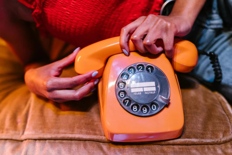 a close up of a person holding an orange telephone, 🦩🪐🐞👩🏻🦳, 7 0 s vibe, customers, sitting down