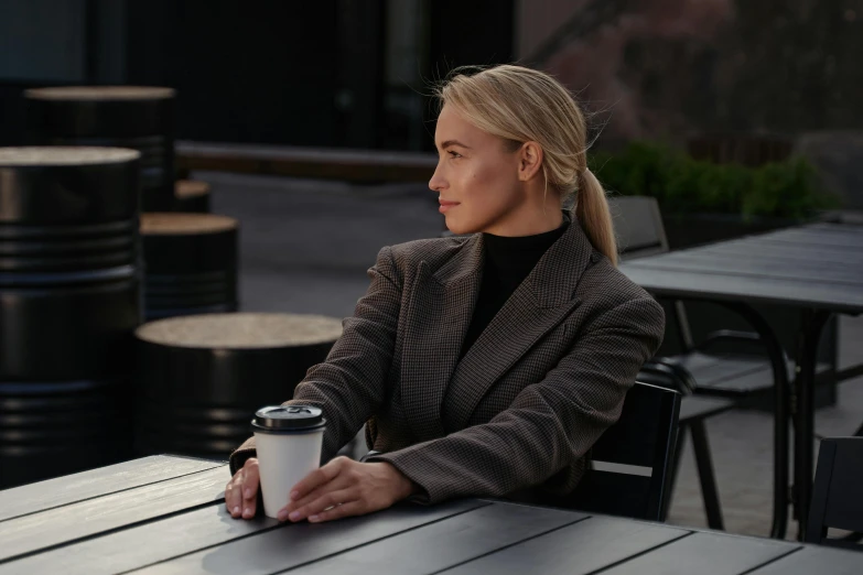 a woman sitting at a table with a cup of coffee, inspired by Louisa Matthíasdóttir, tailored clothing, calm weather, **cinematic, sydney hanson